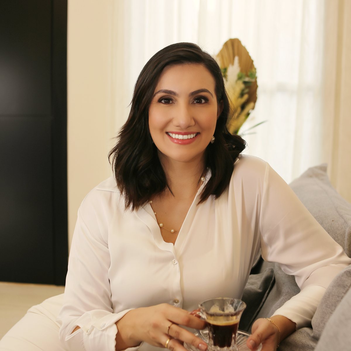 Dra. Anne com uma xícara de café, sentada em um sofá